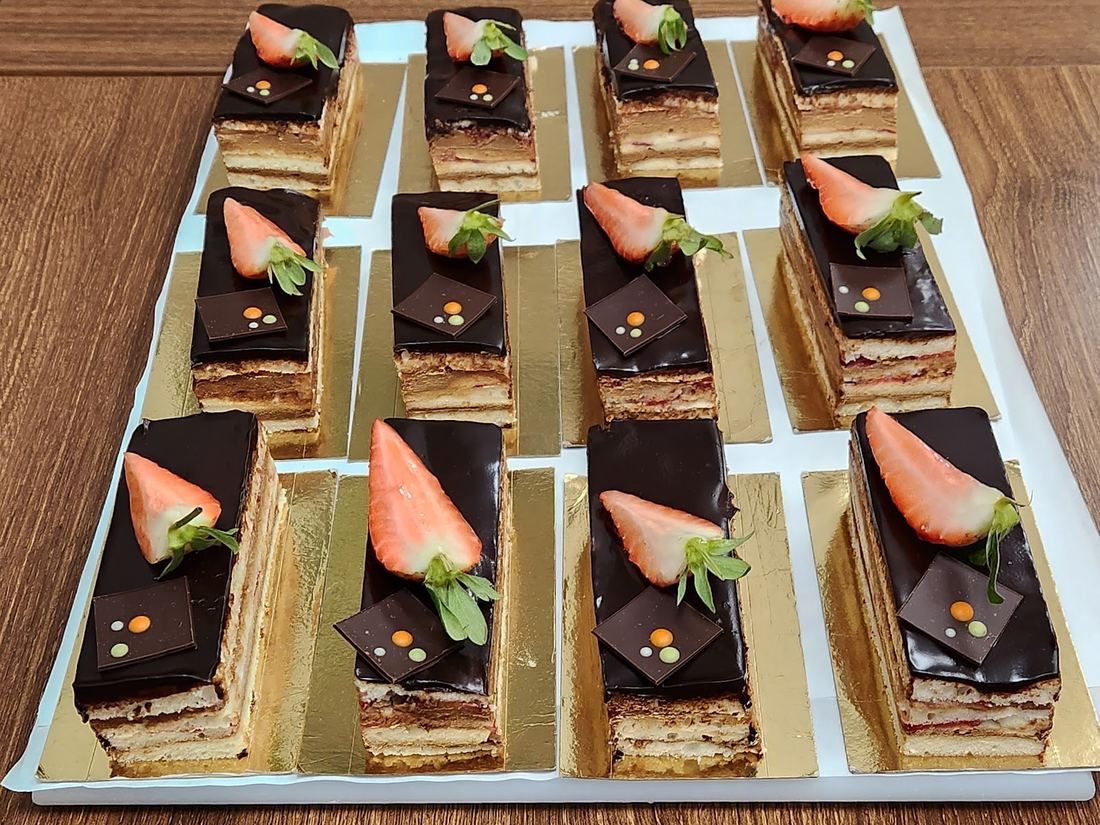 Individual opera cake slices topped with strawberry, set out on a catering tray