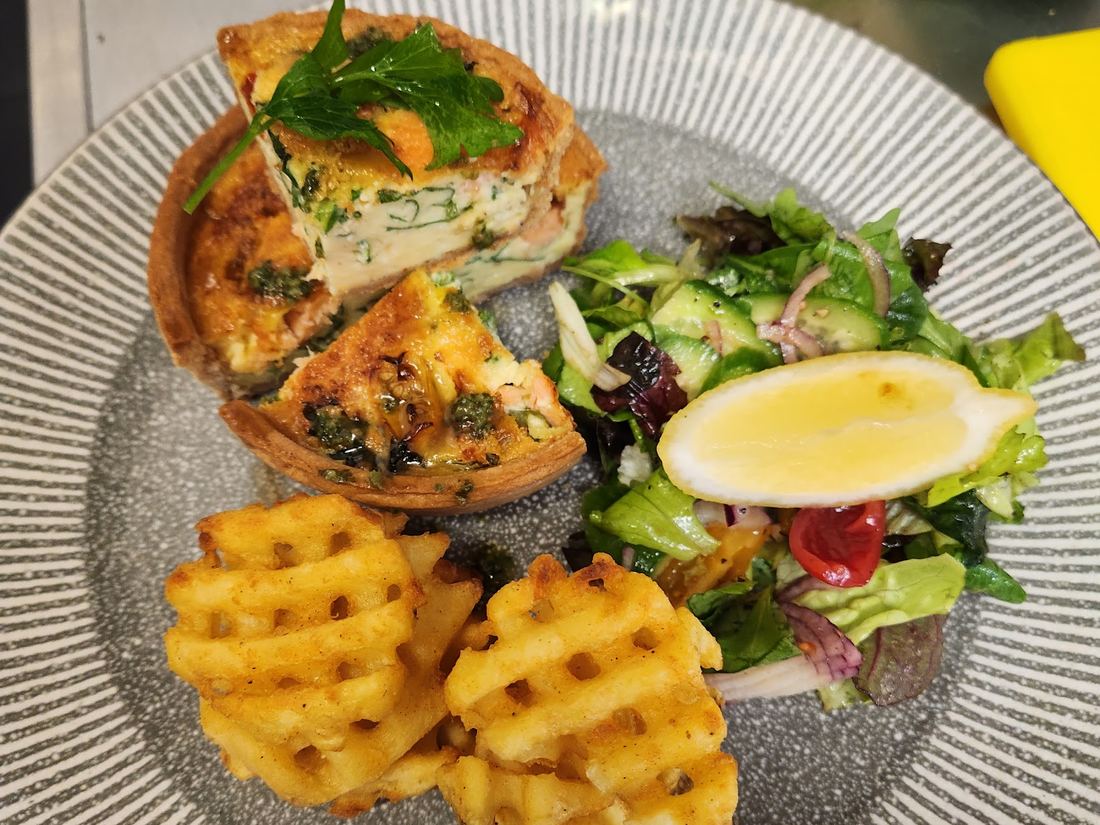 A quiche slice with waffle fries and mixed salad