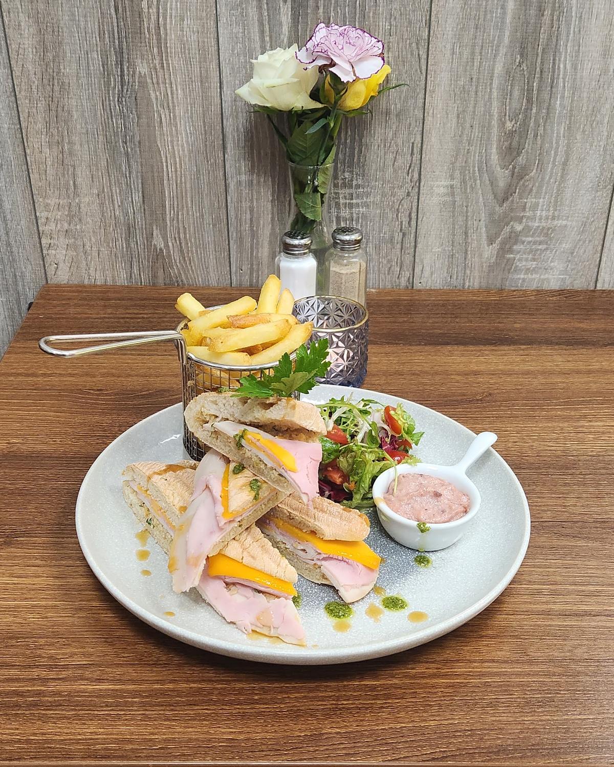 A gourmet deli sandwich with waffle fries, salad and a small vase of flowers